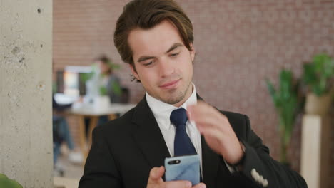portrait-of-young-successful-businessman-using-smartphone-texting-enjoying-browsing-messages-online-on-mobile-phone-connection-running-hand-through-hair