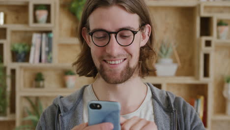 Nahaufnahme-Porträt-Eines-Jungen-Geek-Mannes,-Der-Sein-Smartphone-Nutzt-Und-SMS-Schreibt.-Hübscher-Student,-Der-Online-Nachrichten-Durchstöbert-Und-SMS-Auf-Dem-Mobiltelefon-Sendet-Und-Glücklich-Lächelt