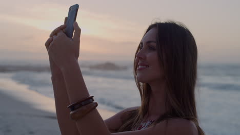 Retrato-De-Una-Joven-Caucásica-Usando-Un-Teléfono-Inteligente-Tomando-Una-Foto-Selfie-En-Una-Hermosa-Y-Tranquila-Playa-Junto-Al-Mar-Al-Atardecer,-Un-Estilo-De-Vida-De-Viaje