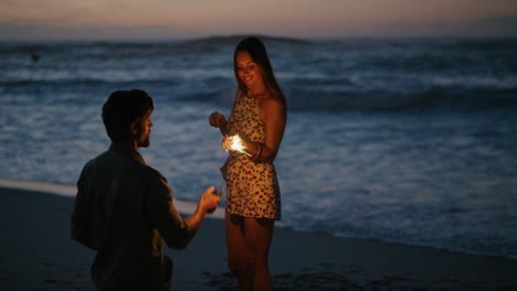 young-man-taking-photo-of-girlfriend-holding-sparklers-dancing-using-smartphone-celebrating-new-years-eve-laughing-playful-together-on-beach-at-sunset-slow-motion