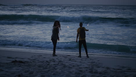 cheerful-friends-on-beach-dancing-celebrating-new-years-eve-waving-sparklers-enjoying-silly-fun-together-in-calm-ocean-seaside-background-at-sunset