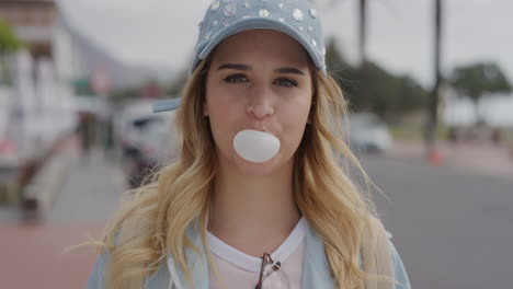 portrait-of-cute-young-blonde-woman-blowing-bubblegum-looking-at-camera-enjoying-urban-beachfront-vacation-on-sunny-urban-street