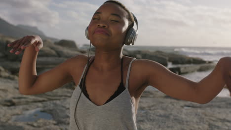Junge-Attraktive-Afroamerikanische-Frau-Mit-Kopfhörern,-Die-Musik-Hört-Und-Glücklich-Am-Strand-Tanzt