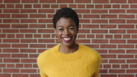 Retrato-De-Una-Mujer-Afroamericana-Segura-De-Sí-Misma-Sonriendo-Alegremente-Usando-Una-Camiseta-Amarilla-Sobre-Fondo-De-Pared-De-Ladrillo