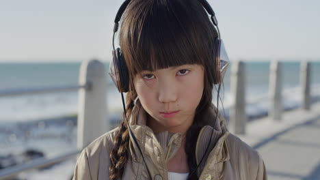 close-up-portrait-beautiful-little-asian-girl-looking-angry-little-kid-upset-wearing-headphones-on-sunny-seaside-beach-slow-motion