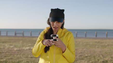 Porträt-Einer-Teenagerin-Mit-Gemischter-Abstammung,-Die-SMS-Schreibt-Und-Mit-Der-Smartphone-Social-Media-App-Surft-–-Glückliche-Überraschung-Am-Strand-Am-Meer