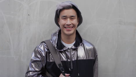 Porträt-Eines-Glücklichen-Jungen-Asiatischen-Studenten,-Der-Lächelt-Und-Den-Entspannten-Urbanen-Lebensstil-Genießt,-Der-Eine-Stilvolle-Silberne-Jacke-Trägt-Und-Echte-Menschenserien-Trägt