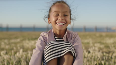 portrait-of-cute-little-mixed-race-girl-sitting-laughing-cheerful-enjoying-sunny-seaside-park-playful-happy