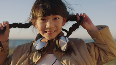 Nahaufnahme-Porträt-Eines-Fröhlichen-Asiatischen-Mädchens,-Das-Fröhlich-Lächelt-Und-Verspielt-Den-Tag-Im-Strandpark-Am-Meer-Genießt-Und-Kopfhörer-Trägt