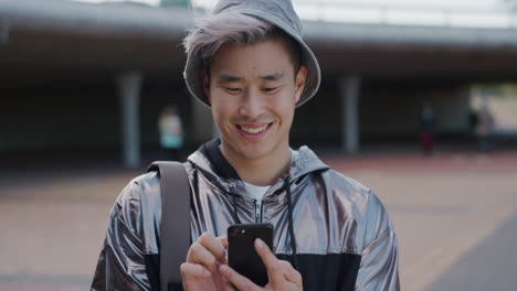 Porträt-Eines-Jungen-Asiatischen-Studenten,-Der-Sein-Smartphone-Nutzt,-SMS-Schreibt-Und-Das-Surfen-In-Online-Nachrichten-Genießt,-Lächelnd,-Zufriedenheit,-Mobiltelefonkommunikation-In-Zeitlupe