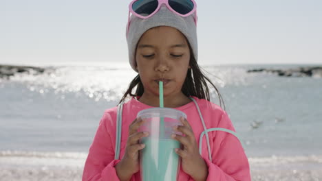 Porträt-Eines-Kleinen-Mädchens,-Das-Am-Strand-Getränke-Trinkt-Und-Eine-Mütze-Und-Rosa-Kleidung-Trägt