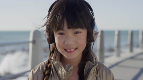 close-up-portrait-cute-little-asian-girl-wearing-headphones-smiling-enjoying-listening-to-music-on-seaside-beach