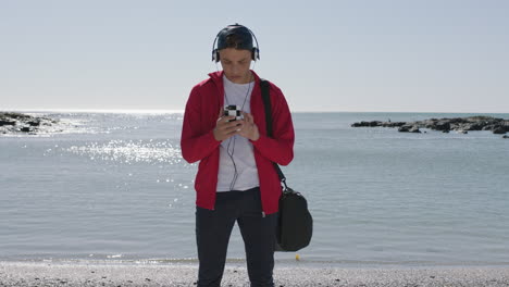 teenage-boy-texting-using-phone-listening-to-music-on-beach