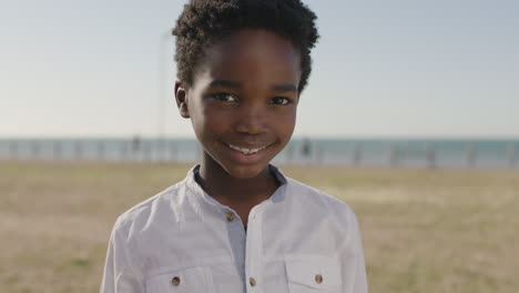 Nahaufnahme-Eines-Porträts-Eines-Süßen-Afroamerikanischen-Jungen,-Der-Fröhlich-Lächelt-Und-In-Die-Kamera-Blickt-Und-Glücklich-Den-Sonnigen-Tag-Im-Park-Am-Meer-Genießt