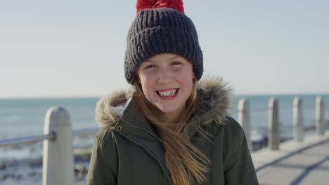 portrait-of-happy-little-girl-on-beach-smiling-cheerful-dressed-warm-wearing-beanie-hat-and-coat