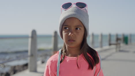 portrait-young-little-mixed-race-girl-looking-serious-contemplative-kid-wearing-beanie-on-sunny-seaside-beach-slow-motion