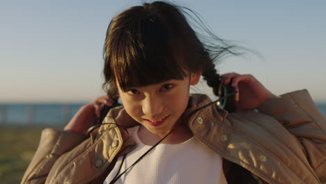 Nahaufnahmeporträt-Eines-Kleinen-Asiatischen-Mädchens,-Das-Kopfhörer-Aufsetzt-Und-Musik-Hört-Und-Den-Tag-Am-Strand-Genießt