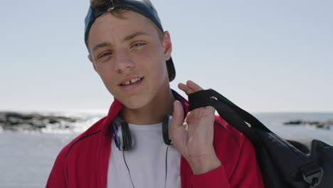 portrait-of-tendy-teenage-boy-wearing-headphones-holding-backpack-on-beach-background
