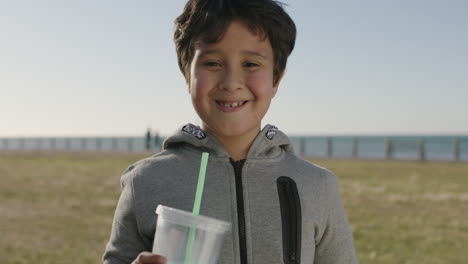 portrait-of-happy-hispanic-boy-smiling-cheerful-at-camera-holding-drinking-milkshake-beverage-at-seaside-park