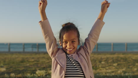 portrait-of-little-mixed-race-girl-happy-cheerful-celebrating-arms-raised-dancing-excited-enjoying-seaside-park