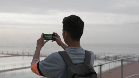 portrait-of-young-asian-man-taking-photo-of-cloudy-seaside-using-phone