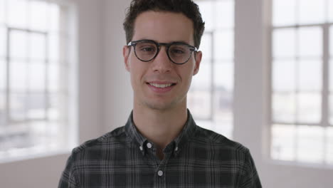 close-up-portrait-of-attractive-young-hipster-man-wearing-glasses-smiling-confident-enjoying-successful-lifestyle-move-independent-male-in-apartment-windows-background
