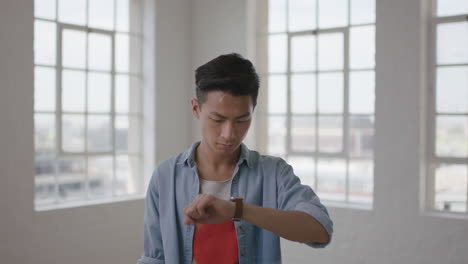 close-up-portrait-of-young-asian-man-student-texting-browsing-messages-using-smart-watch-mobile-technology-in-apartment-windows-background