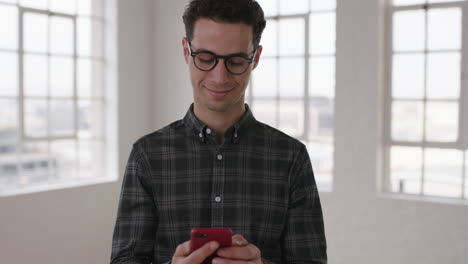 portrait-of-handsome-young-hipster-man-texting-browsing-social-media-using-smartphone-mobile-technology-wearing-glasses-in-new-apartment