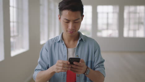 Porträt-Eines-Jungen-Asiatischen-Studenten,-Der-In-Einem-Leeren-Wohnraum-Mit-Smartphone-Mobiltechnologie-SMS-Schreibt-Und-In-Sozialen-Medien-Surft