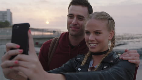 happy-young-couple-posing-for-selfie-photo-using-phone-enjoying-seaside-sunset