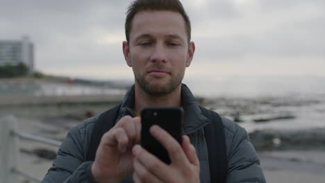 close-up-portrait-of-handsome-man-using-phone-texting-on-seaside-beach