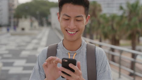 Porträt-Eines-Jungen-Asiatischen-Mannes,-Teenager,-Der-SMS-Nutzt,-Um-Nachrichten-Online-Zu-Verschicken-Und-Urlaub-Auf-Dem-Mobiltelefon-Zu-Teilen.-Kommunikationstechnologie,-Lächeln,-Zufriedenheit,-Städtischer-Hintergrund