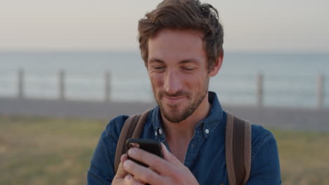 Porträt-Eines-Gutaussehenden-Jungen-Mannes,-Der-Sein-Smartphone-Lächelt-Und-Das-Lesen-Von-Online-Nachrichten-Beim-Surfen-In-Der-Handy-App-In-Zeitlupe-Am-Meer-Genießt