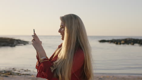 portrait-of-attractive-young-blonde-woman-using-phone-taking-photo-of-beautiful-calm-seaside-on-sunny-beach