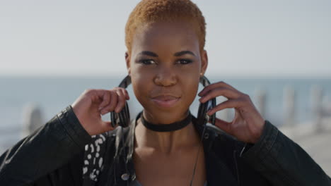 Porträt-Einer-Stilvollen-Afroamerikanischen-Frau,-Die-Kopfhörer-Aufsetzt-Und-Musik-Vor-Einem-Wunderschönen-Hintergrund-Am-Meer-Hört