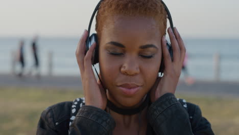 portrait-young-african-american-woman-puts-on-headphones-listening-to-calm-music-enjoying-relaxation-on-beautiful-summer-seaside-day-slow-motion