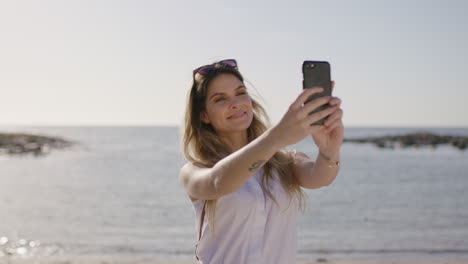 Retrato-De-Una-Encantadora-Mujer-Rubia-Tomando-Selfie-En-La-Playa-Usando-El-Teléfono-Sonriendo-Feliz