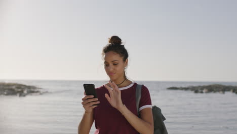 portrait-of-hispanic-woman-using-phone-on-beach-texting-browsing