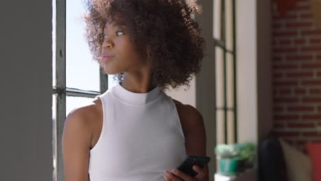 stylish-black-woman-using-smartphone-at-home-browsing-messages-enjoying-relaxed-lifestyle-looking-out-window-african-american-female-texting-on-mobile-phone