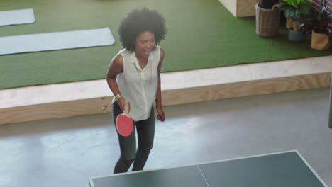 Joven-Mujer-De-Negocios-Afroamericana-Jugando-Ping-Pong-En-La-Oficina-Disfrutando-De-Un-Juego-Competitivo-Divirtiéndose-Durante-El-Almuerzo