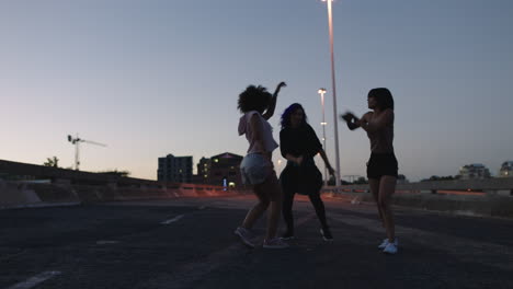 Mujer-Bailando-Felices-Bailarinas-Callejeras-Multiétnicas-Disfrutando-De-Funky-Movimientos-De-Hip-Hop-Realizando-Bailes-De-Estilo-Libre-Juntos-En-La-Ciudad-Al-Atardecer