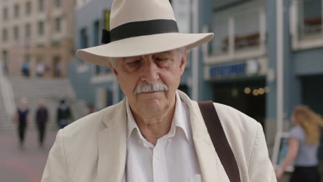 portrait-of-stylish-elderly-man-on-vacation-tourist-looking-serious-wearing-white-suit-and-hat-removes-glasses