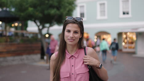 Zeitlupenporträt-Einer-Jungen-Schönen-Frau-In-Rosafarbener-Bluse,-Die-Fröhlich-In-Die-Kamera-Lächelt,-Abends-Im-Städtischen-Hintergrund