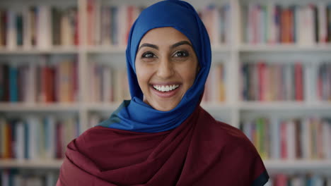 Retrato-Emocionado-Joven-Mujer-Musulmana-Sonriendo-Disfrutando-De-Un-Logro-Educativo-Exitoso-Usando-Hijab-En-El-Fondo-De-La-Estantería-De-La-Biblioteca-Cámara-Lenta