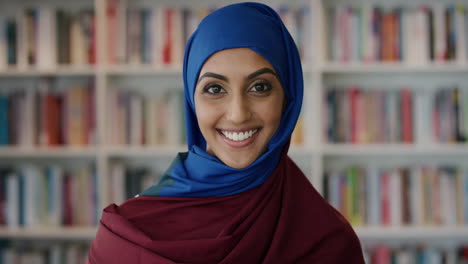 Retrato-Feliz-Joven-Musulmana-Sonriendo-Disfrutando-De-Logros-Educativos-Exitosos-Usando-Hijab-En-El-Fondo-De-La-Estantería-De-La-Biblioteca-Cámara-Lenta