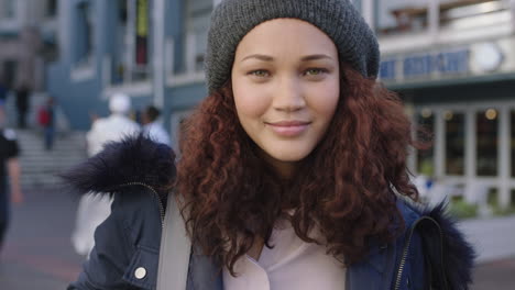 Porträt-Einer-Schönen-Frau-Gemischter-Abstammung-Mit-Krausem-Haar,-Die-Selbstbewusst-Lächelt-Und-Eine-Pelzmantel-Mütze-Im-Geschäftigen-Städtischen-Hintergrund-Trägt