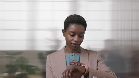 portrait-of-successful-african-american-business-woman-checking-messages-using-smart-watch-mobile-technology-black-independent-female-working-in-office-background