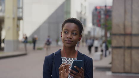 Retrato-Profesional-Afroamericana-Mujer-De-Negocios-Usando-Un-Teléfono-Inteligente-Usando-Auriculares-Navegando-En-Línea-Revisando-Mensajes-Disfrutando-Escuchando-Música-En-La-Ciudad