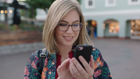 Porträt-Einer-Jungen-Blonden-Frau,-Die-Mit-Einer-Smartphone-Social-Media-App-SMS-Schreibt-Und-Lächelt-Und-Eine-Brille-Im-Städtischen-Hintergrund-Trägt