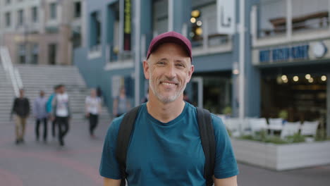portrait-of-mature-attractive-caucasian-tourist-man-wearing-hat-looking-at-camera-smiling-city-background